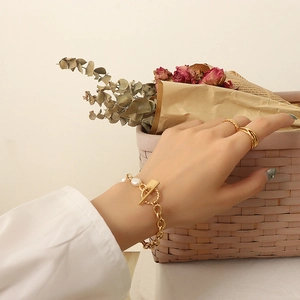 Gold chain bracelet with freshwater pearls and stackable rings on a floral background