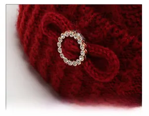 Detail of red knit hat featuring a rhinestone buckle and a matching yarn bow design