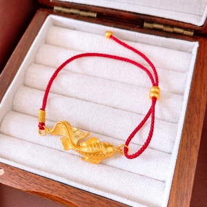 Detail shot of a golden koi fish pendant with intricate scales on a red woven bracelet
