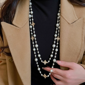Close-up of double-layered pearl necklace featuring sparkling gold cross charms on a model