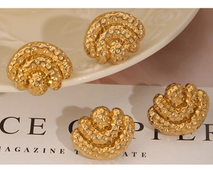 Detail of vintage gold fan-shaped earrings with hammered texture on a ceramic tray