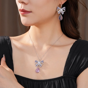 Close-up of bow necklace and earrings set with purple teardrop crystals on model