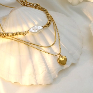 Detailed view of layered gold heart necklace with pearls on a white shell and silk fabric