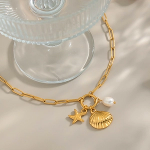 Detail of gold paperclip chain necklace with starfish shell and baroque pearl charms