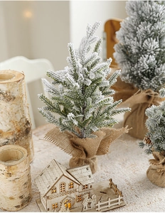 Close-up of mini snowy Christmas tree with burlap base and glowing wooden house decor