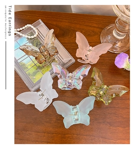 Exquisite butterfly hair claw clips in six colors including amber and olive on a wooden desk