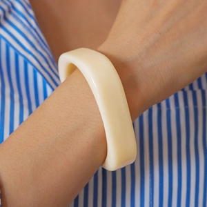 Macro detail of chunky ivory resin square bangle on model wearing striped shirt