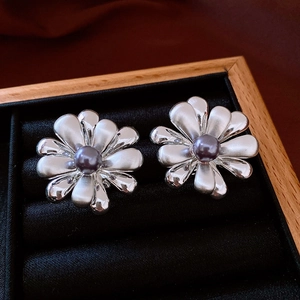Macro detail of silver flower earrings with deep purple pearl set in a wooden jewelry box