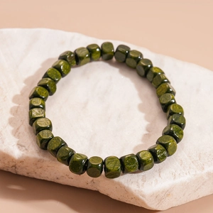 Detail view of square green wooden beads with natural grain on an organic stone base