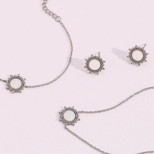 Detailed view of silver sun-shaped jewelry set with opal stone on a pink texture surface