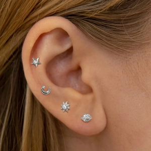 Detailed view of silver star, moon, sun, and planet stud earrings on ear model