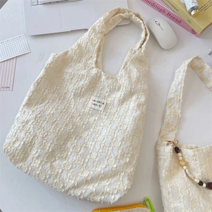Close-up of off-white lace tote bag with 3D floral texture and brand label