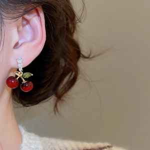 Détail de boucles d'oreilles cerise en résine rouge avec feuille verte et zircons fins