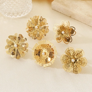 Gros plan de bagues fleurs évidées dorées avec perles blanches sur fond texturé beige
