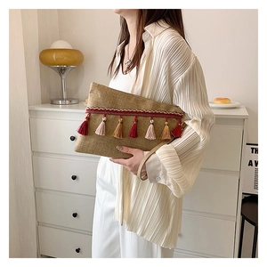 Close-up of linen envelope clutch with colorful tassels held by a model in a minimalist room