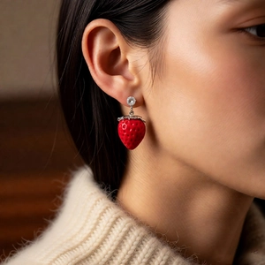 Close-up of a model wearing red strawberry enamel earrings with zircon accents and silver leaves