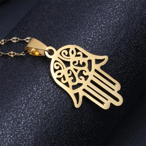 Detailed macro view of a gold Hamsa hand pendant on a stainless steel chain necklace
