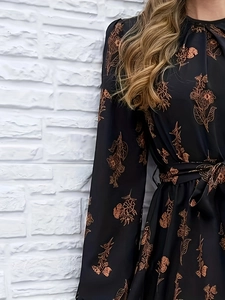 Elegantes florales Maxikleid mit langen Ärmeln und Taillengürtel vor weißer Wand