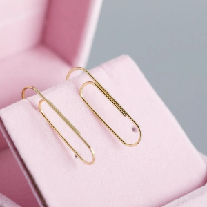 Minimalist gold paperclip earrings displayed on a pink velvet jewelry box cushion