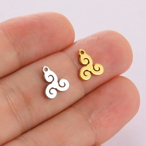Polished stainless steel triskele pendants in silver and gold displayed on a finger