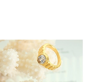Detailed close-up of a wide gold-plated ribbed ring with a central zircon on coral decoration