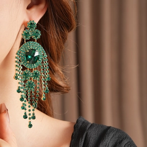 Dettaglio di orecchini vintage dorati con frange di strass verdi indossati da modella