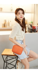 Detail of orange V-quilted small crossbody bag with gold chain strap on a wooden stool