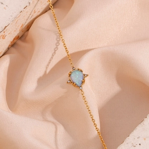 Detailed close-up of golden teardrop opal pendant necklace with diamonds on champagne silk