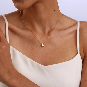 Close-up of gold-plated balloon letter K pendant necklace on a model with white top