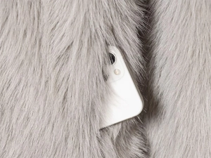 Detail of hidden side pocket on grey faux fur hooded coat with a smartphone inside