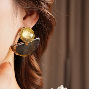 Close-up of bohemian resin fan earrings with gold studs worn by a model in soft light