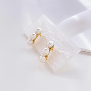 Macro shot of minimalist gold pearl earrings with three pearls in curved row on marble