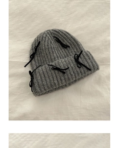 Detailed texture of gray knit beanie with black ribbon bows on a white fabric background