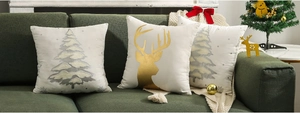 Detail of Christmas pillow covers with gold deer and silver tree motifs on green sofa