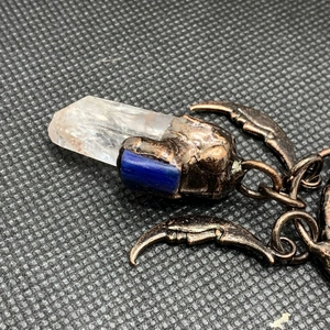 Detailed close-up of a bronze sun god pendant with blue stone and clear crystal point