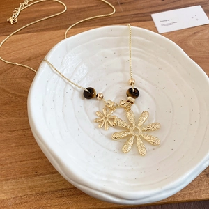 Detail of tiger eye bead and gold layered flower pendant necklace on ceramic dish