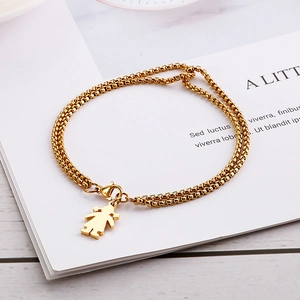 Dettaglio di un bracciale dorato a doppia catena con un delicato ciondolo a forma di ragazza