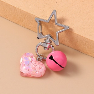 Detail of pink resin heart pendant with sequins, silver star clip, and metal bell