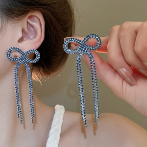 Detail showing blue rhinestone bow earrings with long tassels on model's ear
