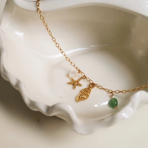 Detail of a gold ocean starfish necklace with pearl and green jade in a shell dish