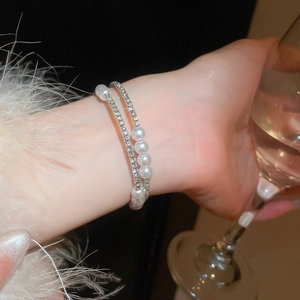 Detail of layered bracelet featuring sparkling rhinestones and round pearls on a female wrist