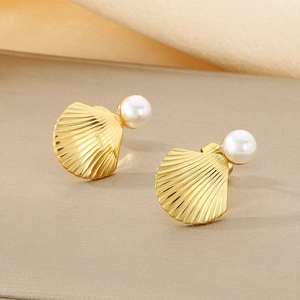 Macro detail of fan-shaped shell gold earrings with white pearl inlay on textured fabric