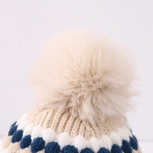 Detalle macro del pompón beige y la textura de punto grueso a rayas del gorro de invierno