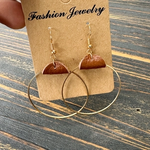 Hand holding minimalist gold round earrings with brown leather accents on a card