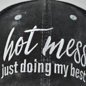 Close-up of white hot mess embroidery on dark gray washed cotton ponytail baseball cap