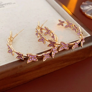 Gros plan de boucles d'oreilles C dorées avec papillons en gemmes mauves sur plateau