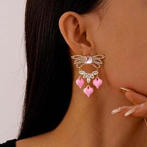 Close-up of elegant gold drop earrings with pink zircon hearts and sparkling crystals