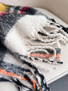 Close-up of the woven plaid scarf featuring multi-color checkered texture and soft fringe