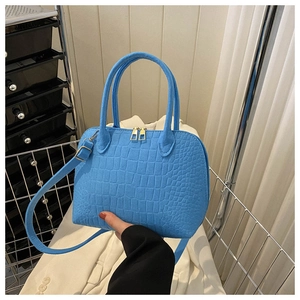 Detail of light blue shell bag with crocodile texture, gold zipper and top handles