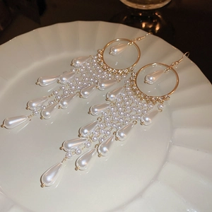 Detailed view of gold tassel earrings with pearls and crystals on a ceramic plate